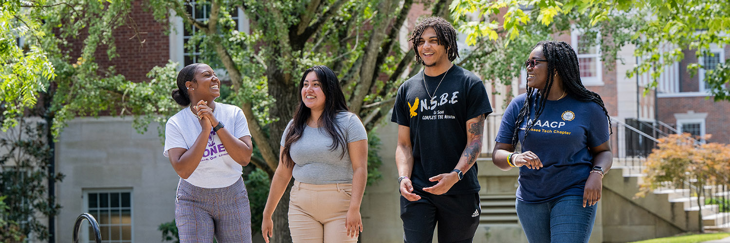 A group of four students walking side by side along the Main Quad laughing with one another. 