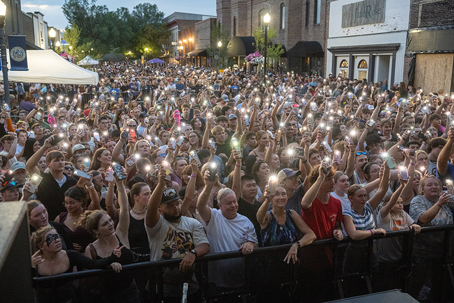 A crowd of poeple holding their cell phones up with flash lights on during a evening concert.