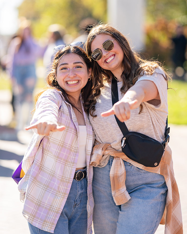 Two students giving a happy wings up to the camera.