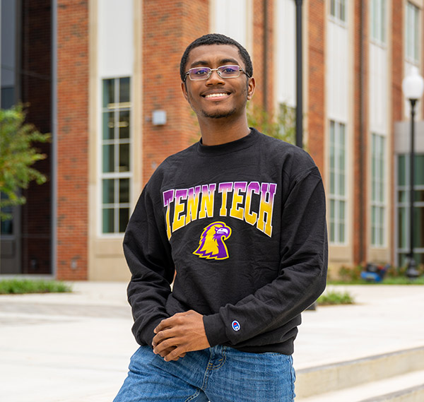 Trevon Collins posting next to the AEIB, smiling at the camera.