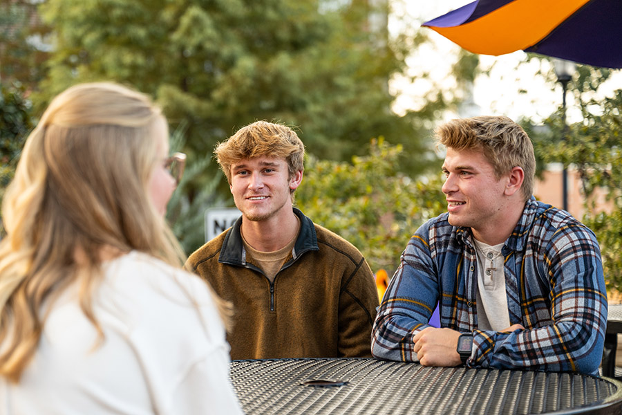 Three students talking at a table on the Plaza.