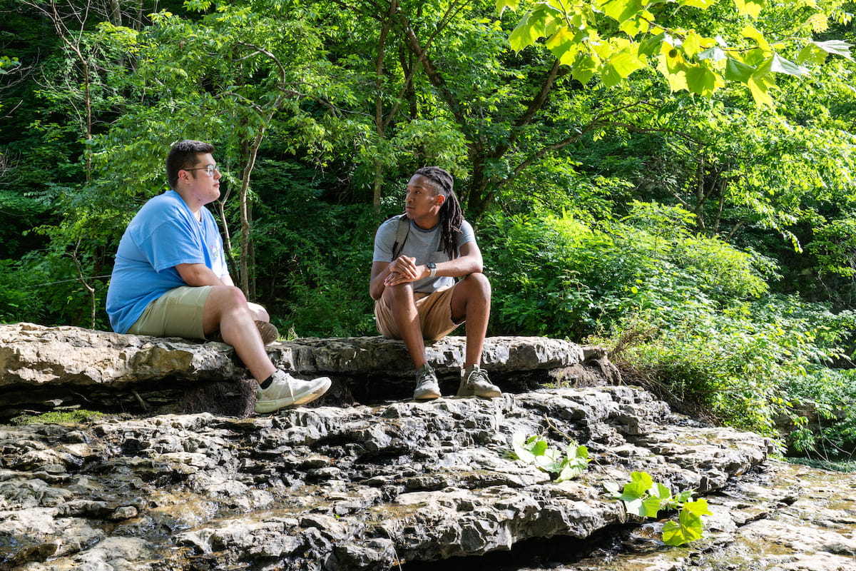 Two students sit beside a rocky stream during a field-based environmental science experience.