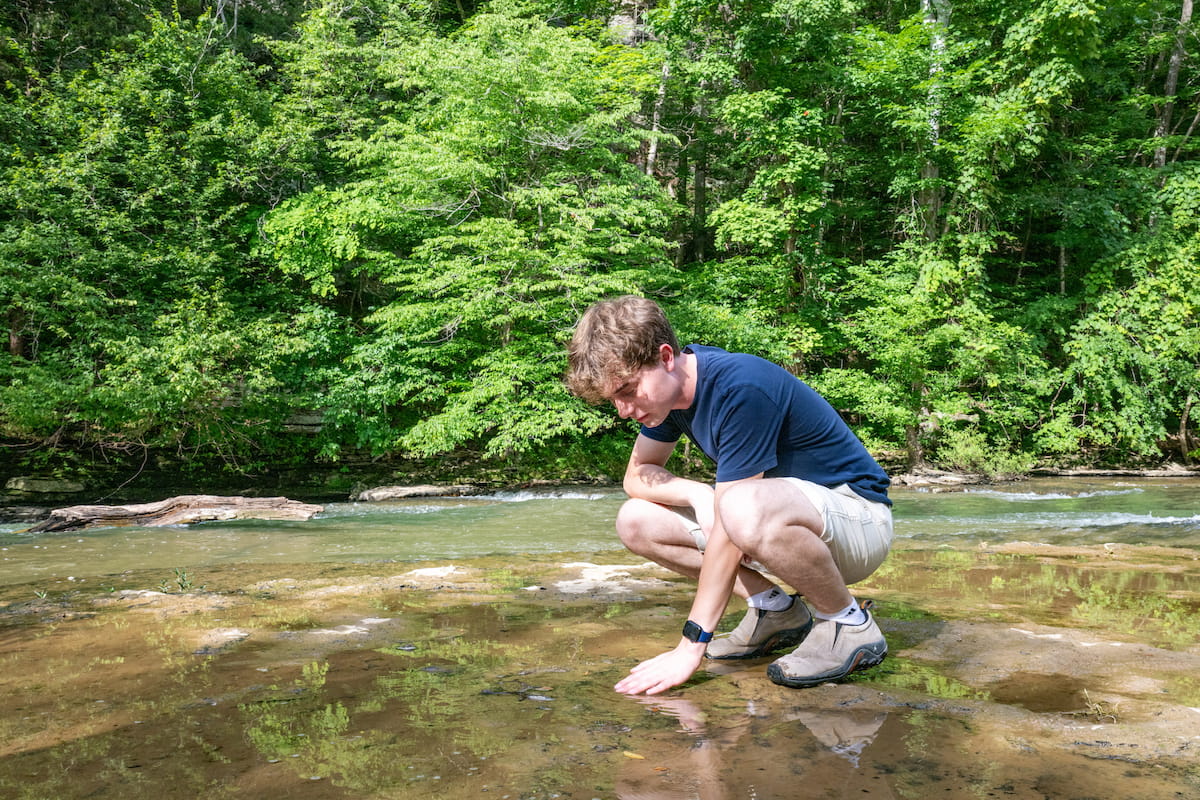 Student examines shallow stream water during a field-based environmental science activity.