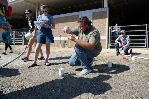 Students observe a hands-on soil testing demonstration during an outdoor field laboratory activity.