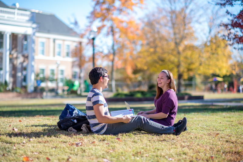 Two students taking notes while sitting in grass.