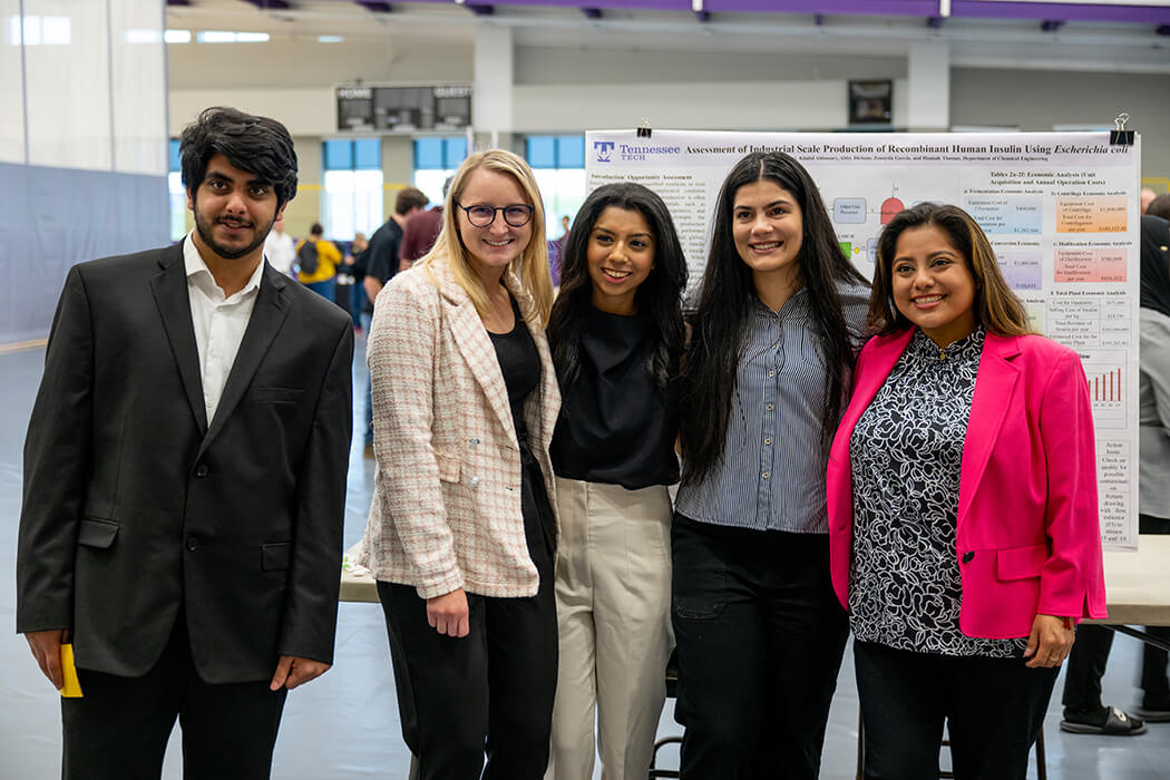 A photo of team of 4 students and their advisor presenting their capstone project