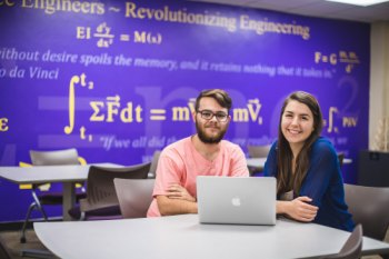two students sitting with laptop smiling