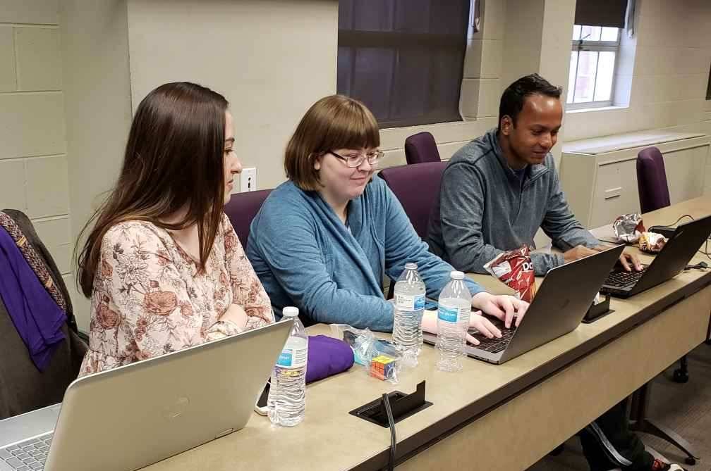 three students in lecture hall working on laptops