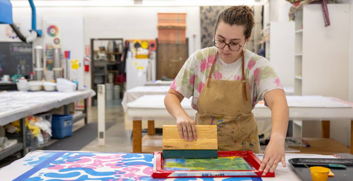 A student creates bold, abstract designs through screen printing in a hands-on studio environment.