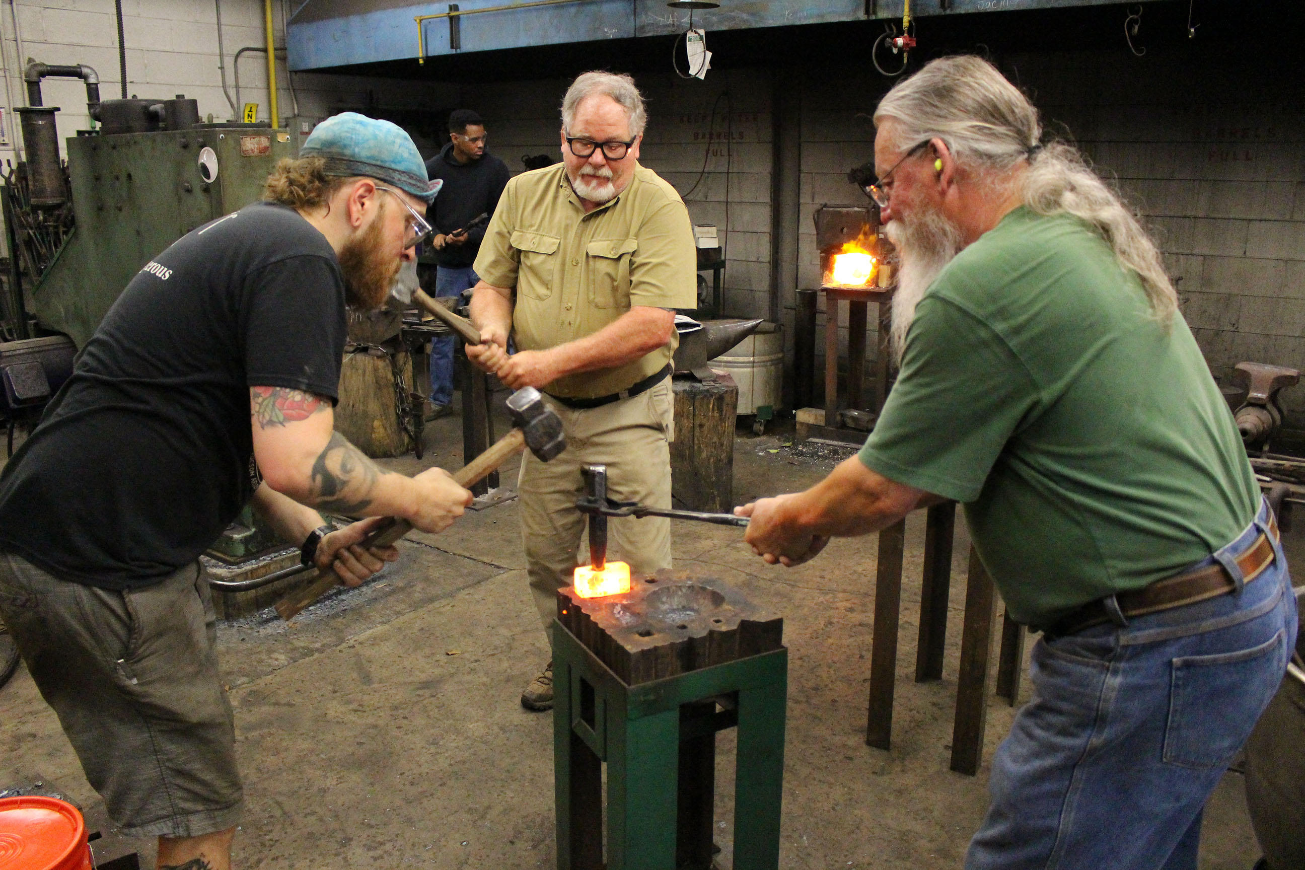 Three men taking turns hammering a heated piece of metal