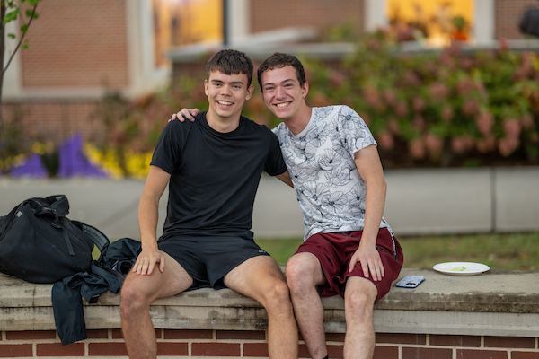 Two students with their arms around each other smiling at the camera.