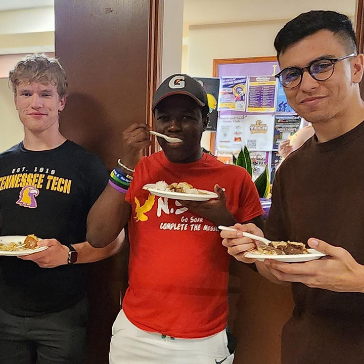 Three students posting for the camera as they eat food from plates.