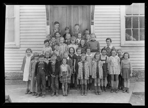 Black-and-white image of school children and teachers in front of a school in the mid-19th century