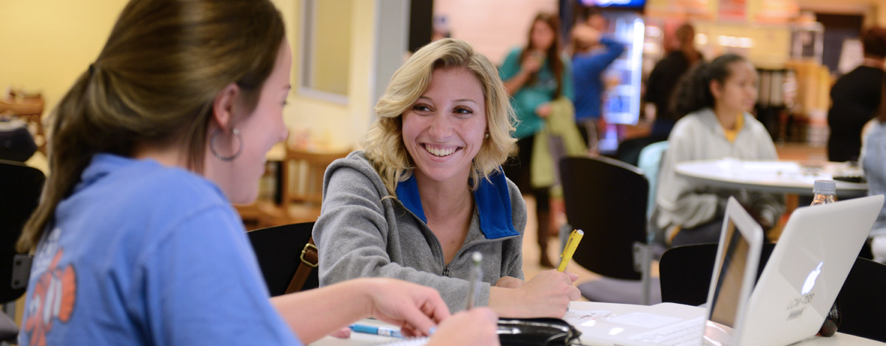 two females studying at a table with laptops