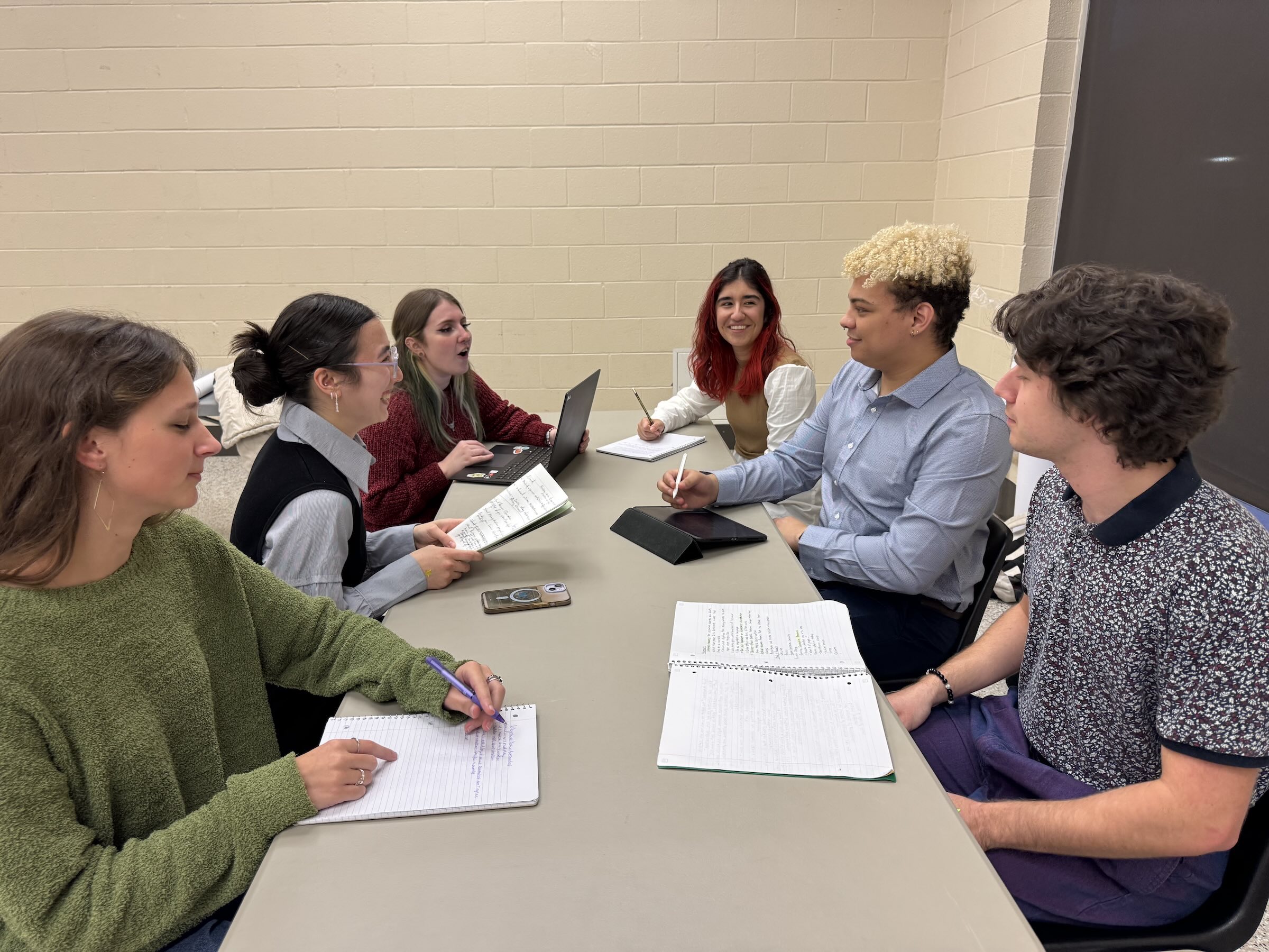 Students sit around a table with open papers and books. 