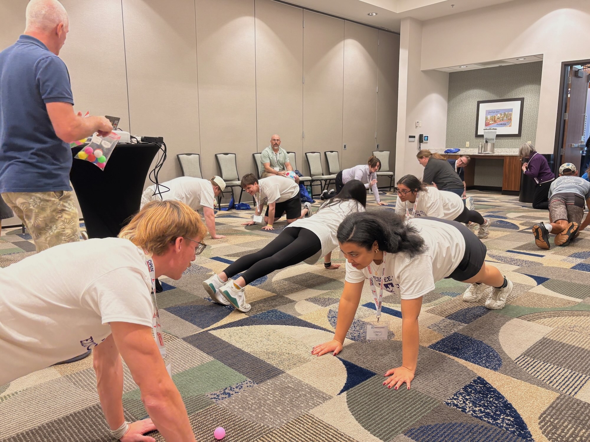 Students do push-ups in a conference room as others look on. 