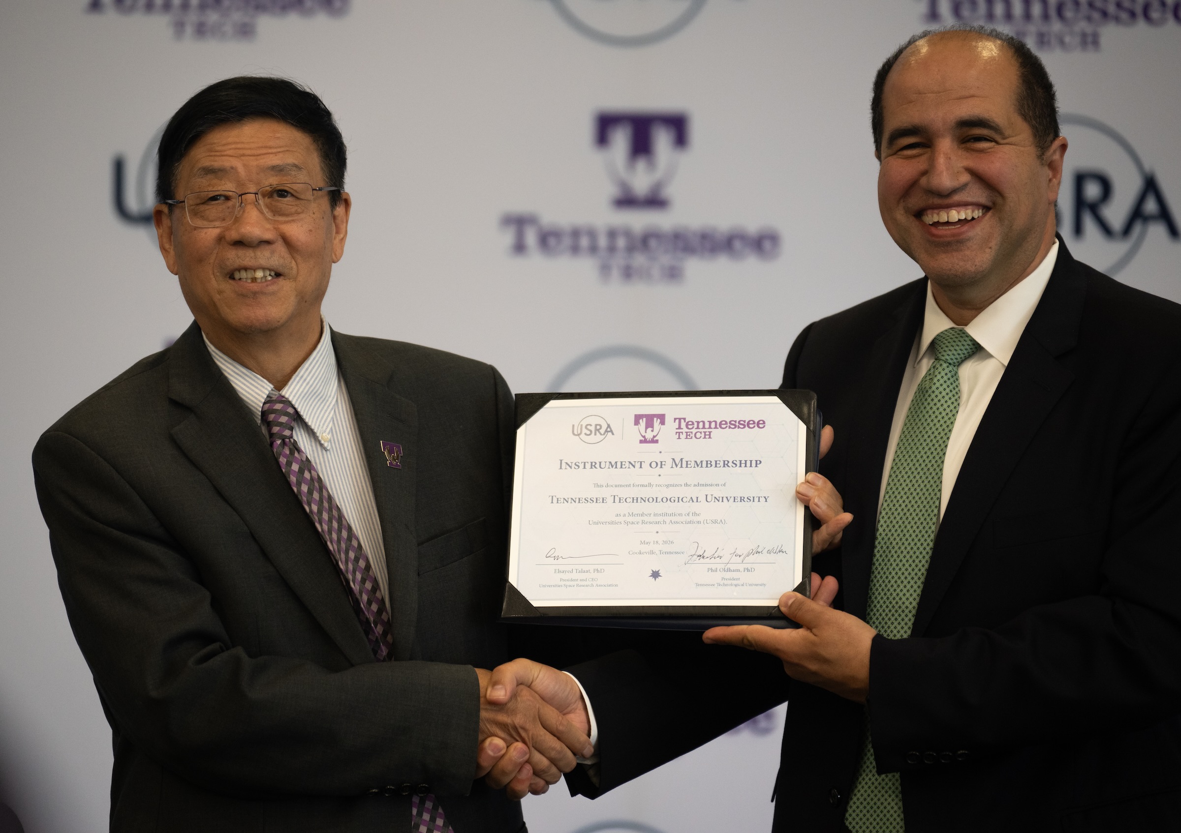 Two men shake hands and smile while holding a certificate. 