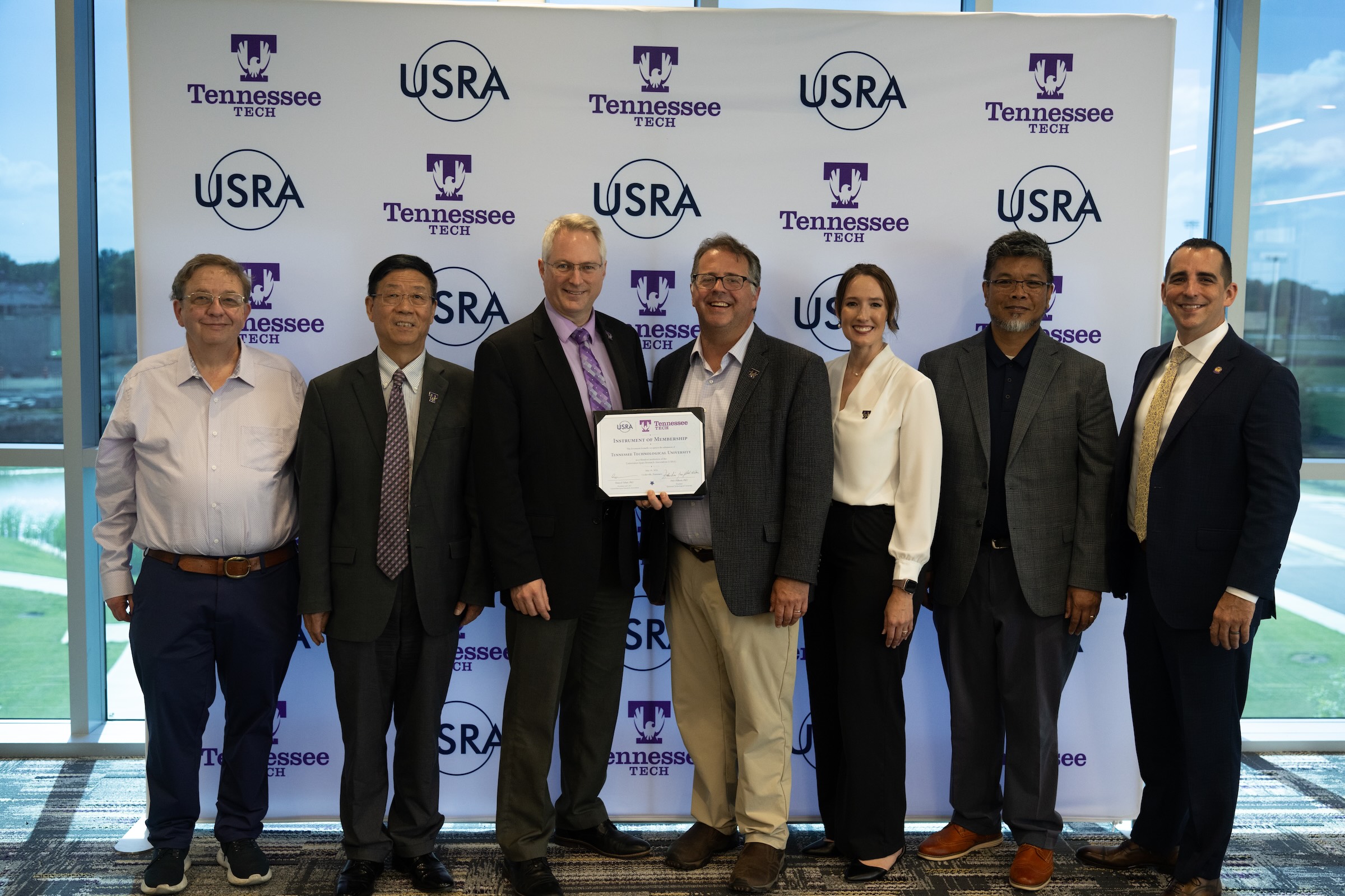 Seven individuals smile in a line and hold a certificate. 