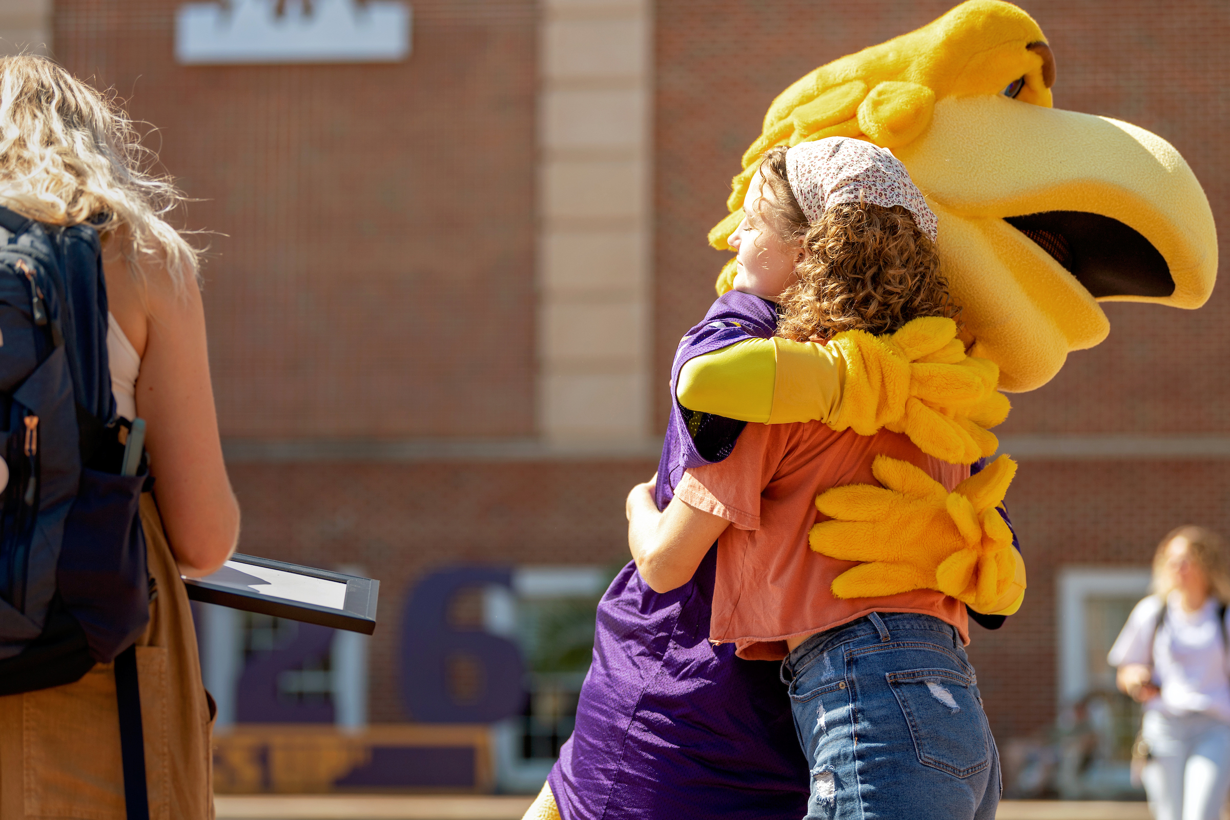 A female-presenting student in jeans and a t-shirt warmly hugging Awesome Eagle during Week of Welcome