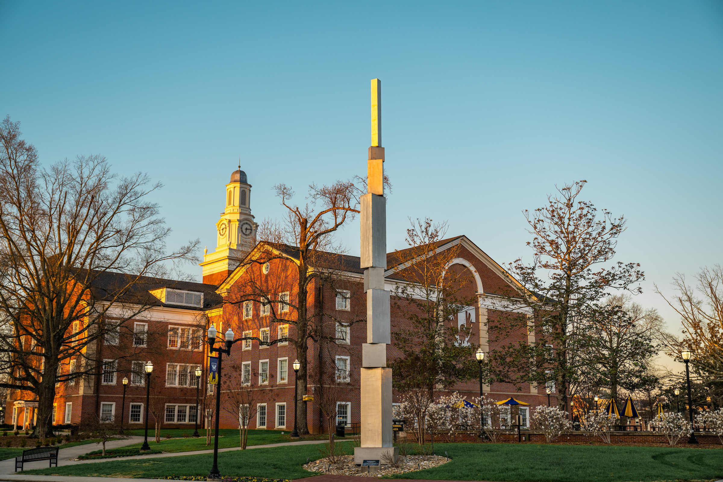 a tall sculpture ascending into the sky beside Derryberry Hall at sunset