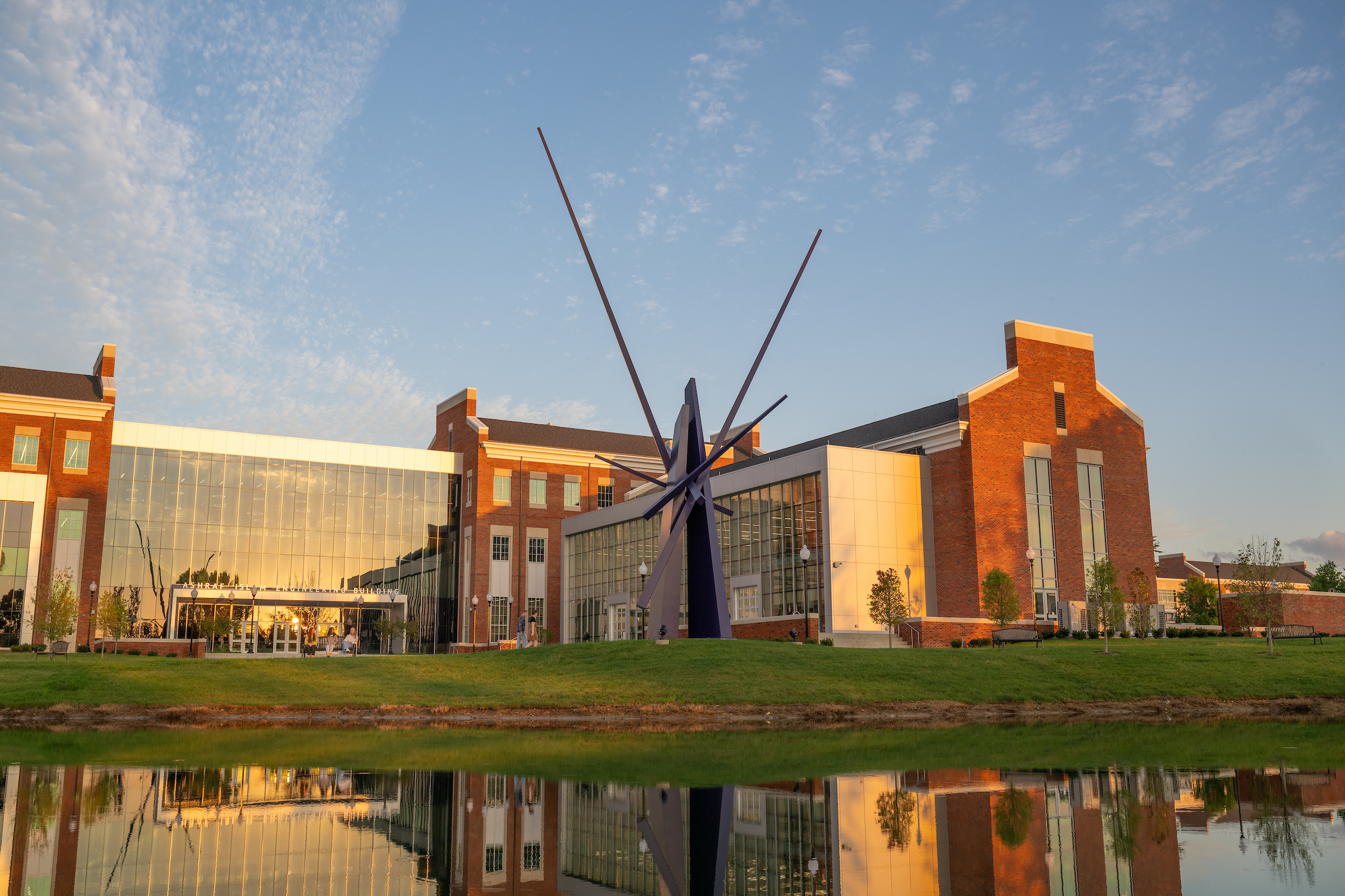 The Ashraf Islam Engineering building at sunset, with a sculpture and a pond in the foreground