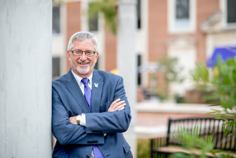 A horizontally orientated photo of President Phil Oldham leaning against a pillar