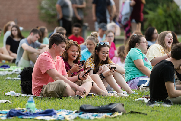 A group of students sitting on the ground, interacting with their phones.