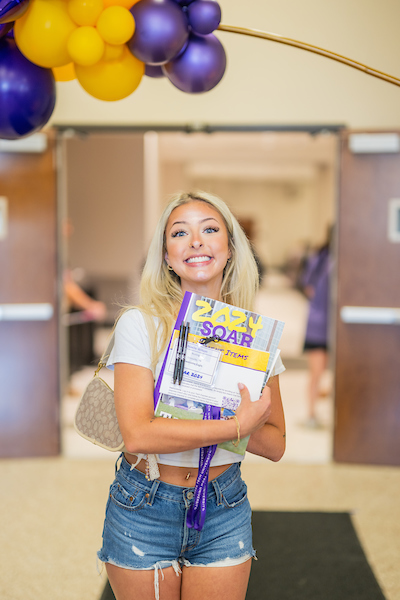 A Freshmen student holding out event materials and giving a big smile to the camera.