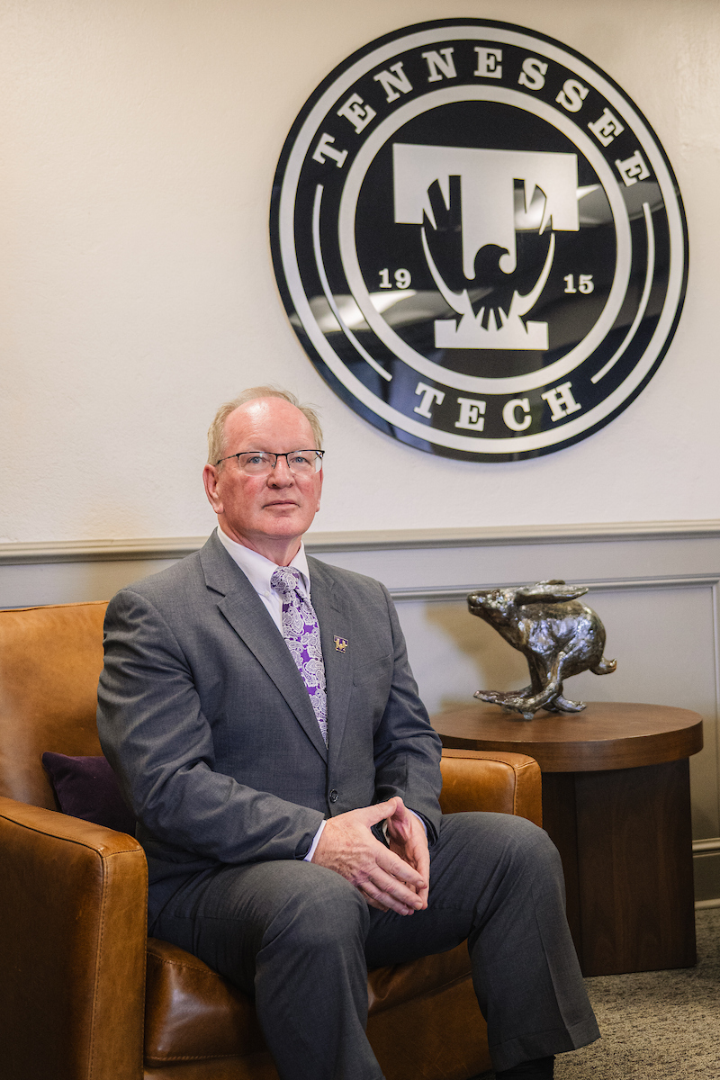Photo of Provost Latour sitting in a tan chair with the Tennessee Tech seal behind him. 