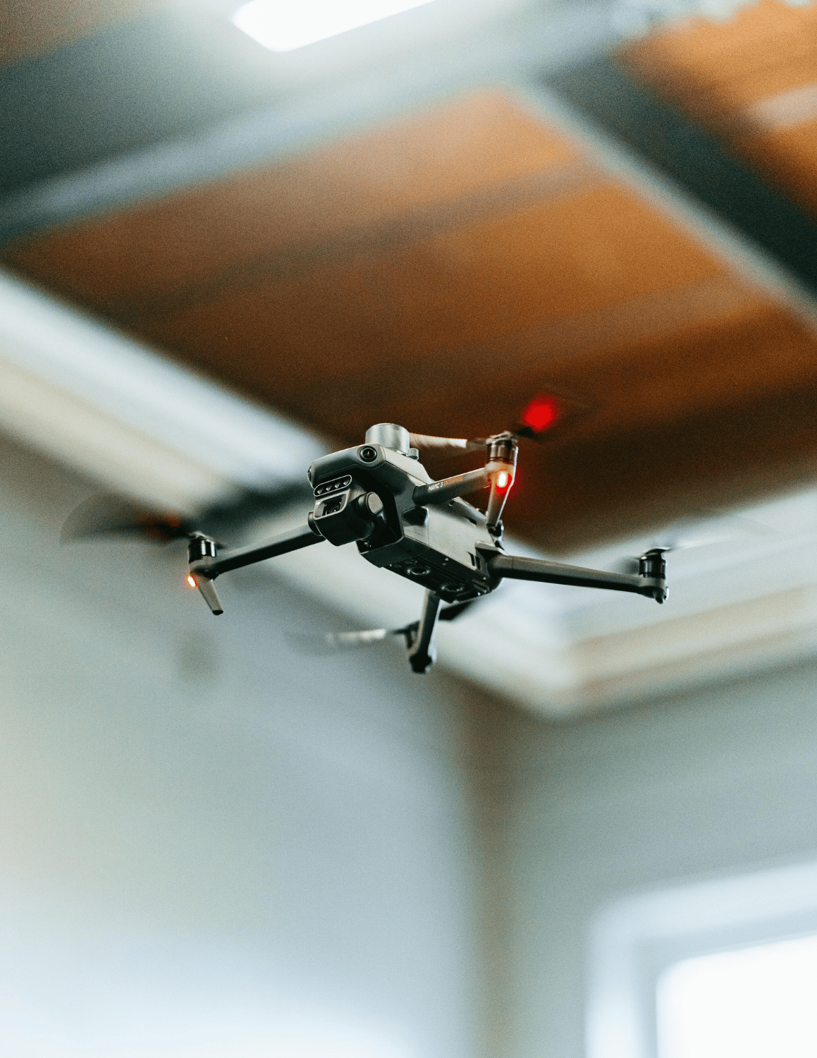 A small black quadcopter drone flying indoors against a softly blurred background.