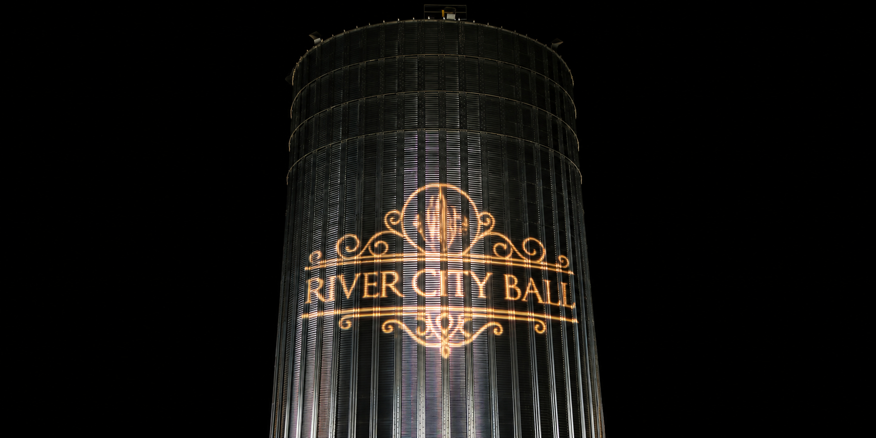 River City Ball logo in white projected on to a silver silo at night.