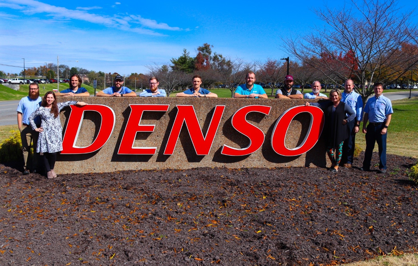 DENSO sign surrounded by employees who are Tech graduates