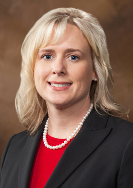Portrait of Jennifer Taylor - she has shoulder-length blonde hair and is wearing pearls, a red blouse, and black blazer
