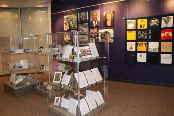 Photo of glass display cases with photographs and text and a canvas photo display on the purple wall behind it.