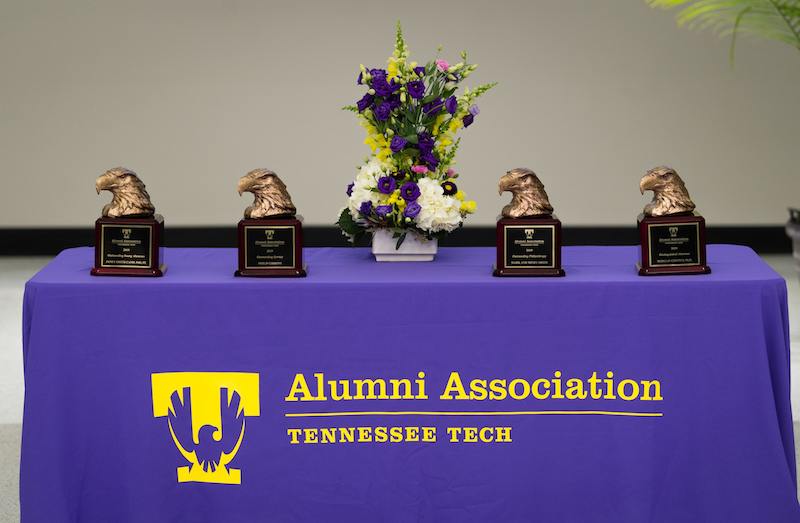 Four golden eagle head awards sit on a table with a purple table cloth that reads "Alumni Association Tennessee Tech"