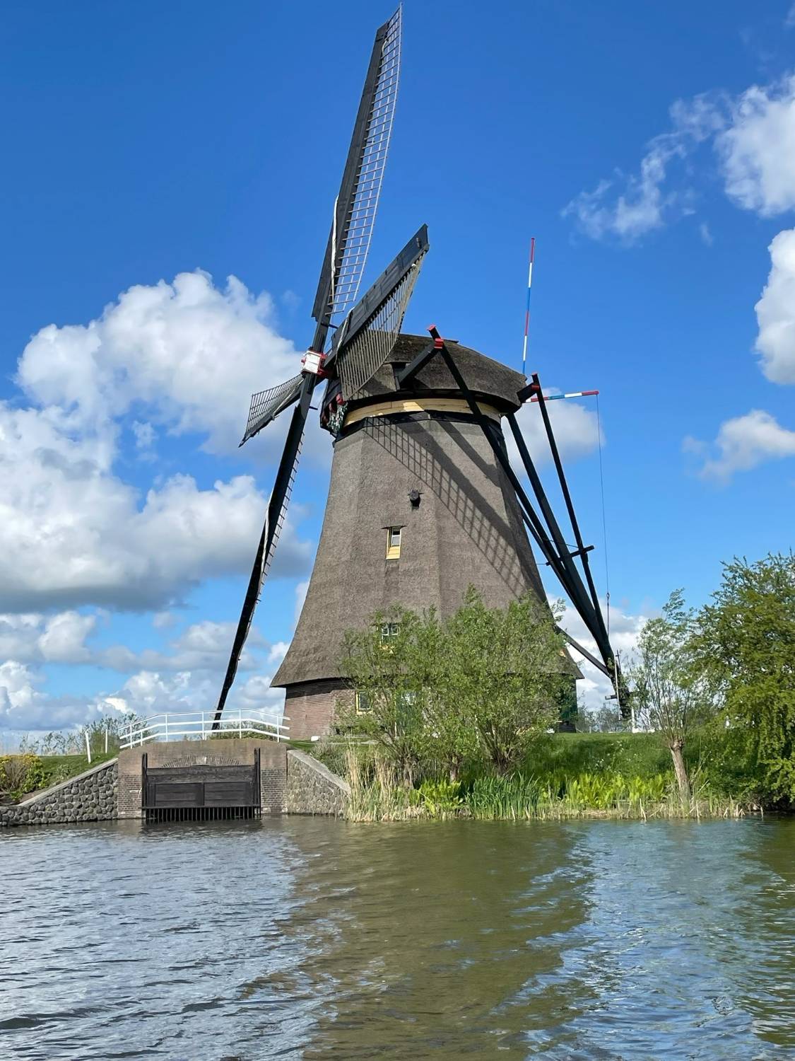 windmill by a body of water on a partly cloudy day 